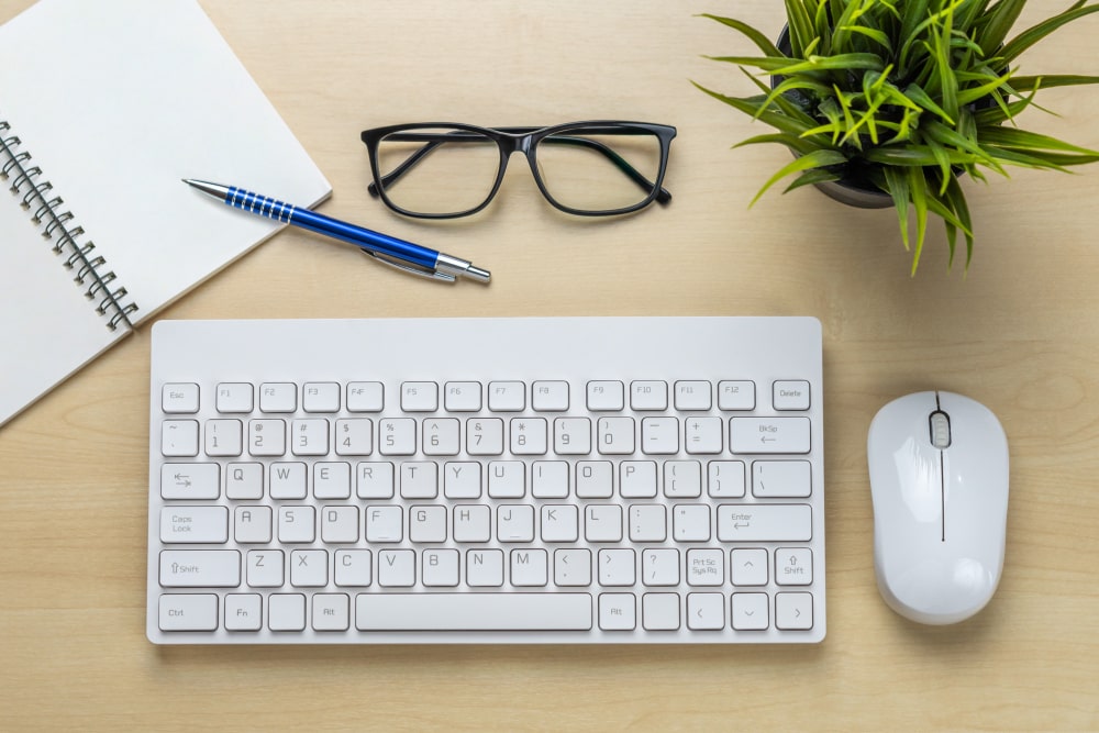 Un clavier PC blanc et une souris sur un bureau en bois clair.